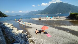 Een strand met mensen die zonnebaden en zwemmen, rotsachtige oevers en bergen op de achtergrond.