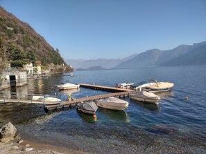 Un lago tranquilo con barcos amarrados a un muelle, rodeado de montañas y cielos despejados.