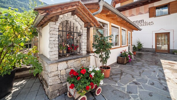 Ein Steinhaus mit Holzdach, schmiedeeisernem Tor und Blumentöpfen.