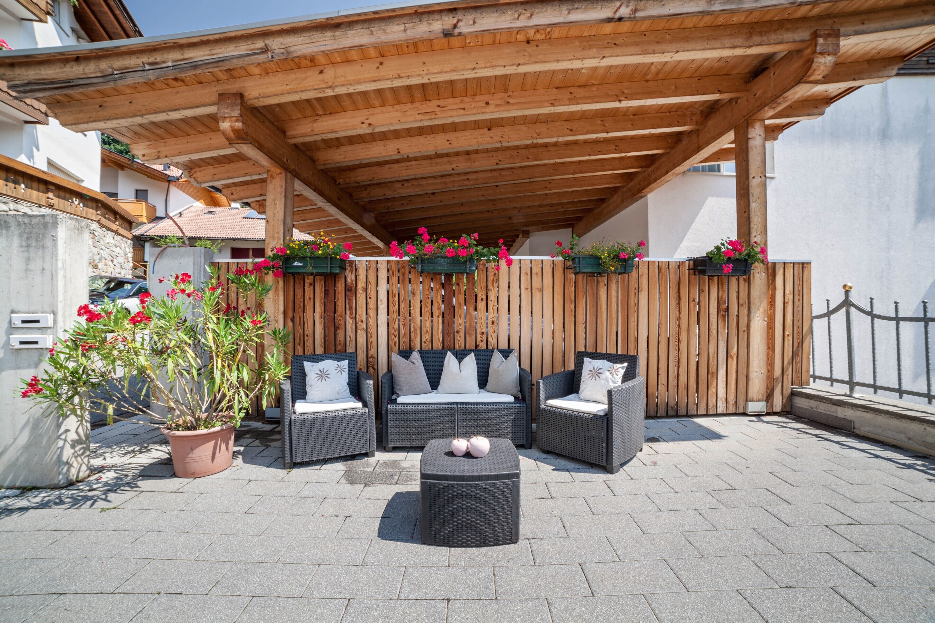 An outdoor patio with wicker furniture, a wooden pergola, and potted plants.