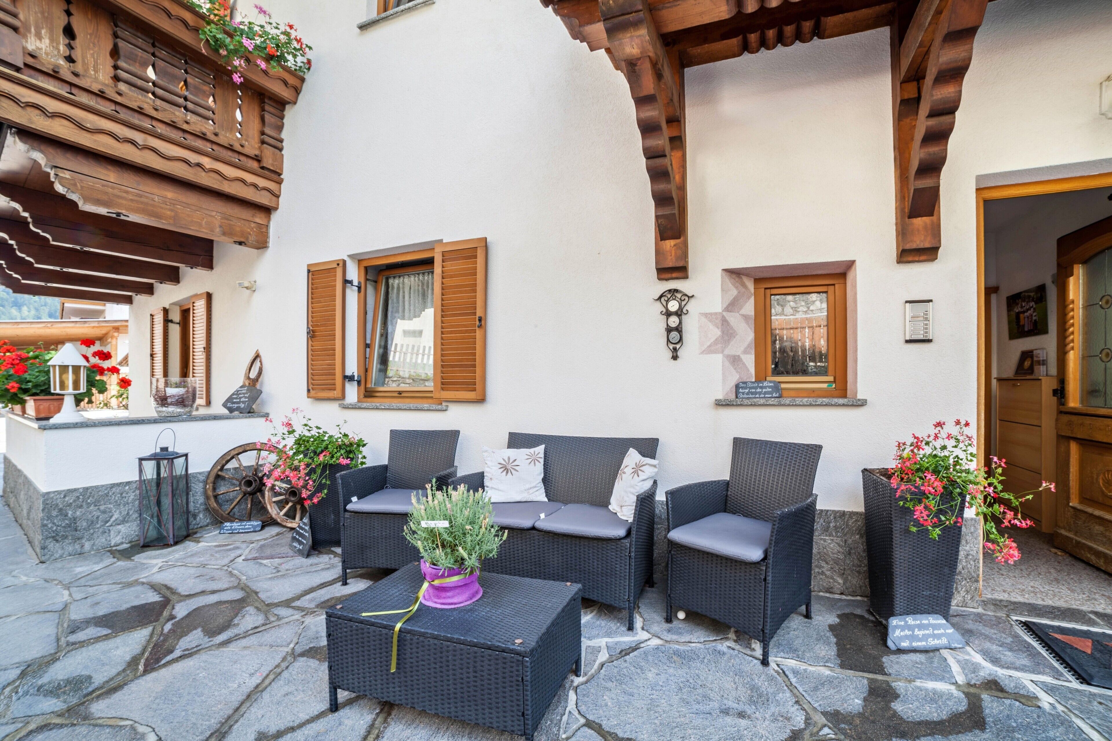 An outdoor seating area with wicker furniture, stone flooring, and wooden beams.