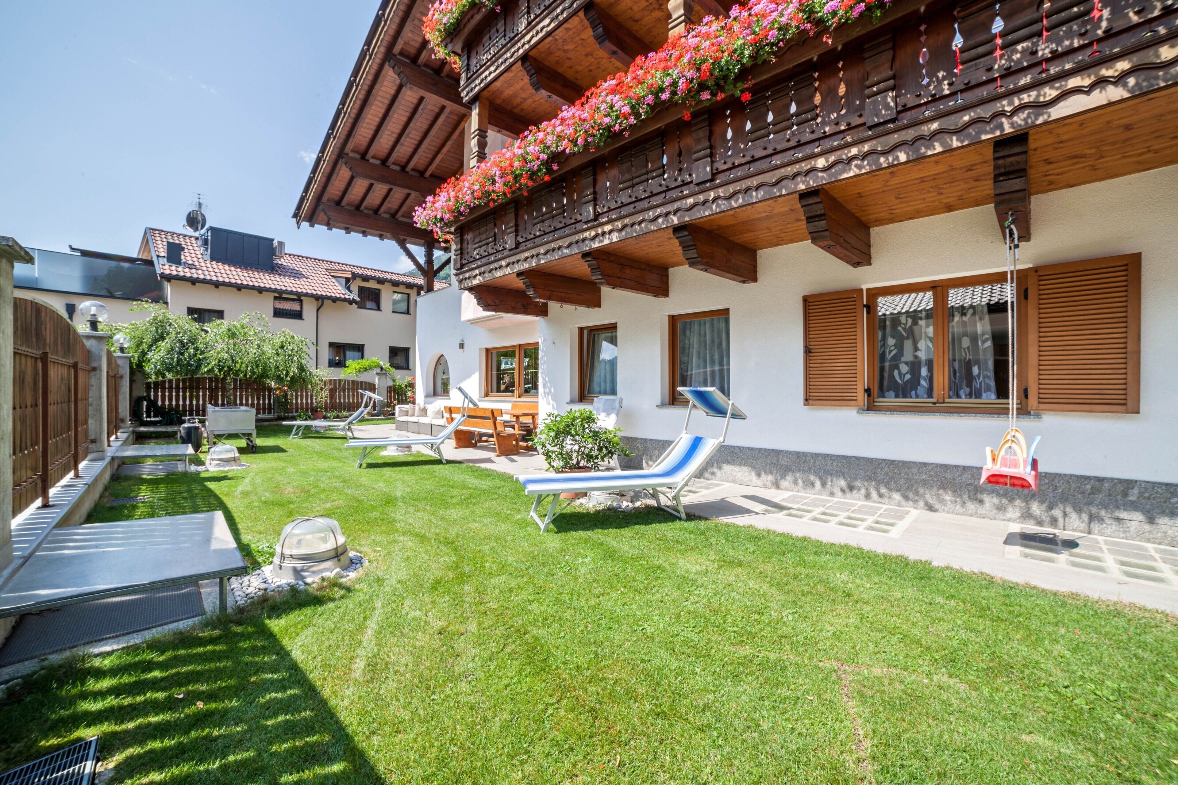 A traditional chalet with a wooden balcony, a well-maintained lawn, and outdoor furniture.