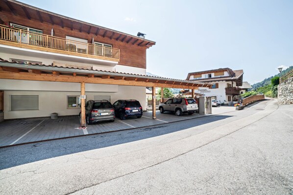 A building with a wooden balcony, a covered parking area, and a sign indicating a restaurant.