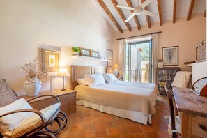 A bedroom with a bed, a chair, a table, a ceiling fan, and a window. - Spacious townhouse in the heart of Sóller. (Soller)