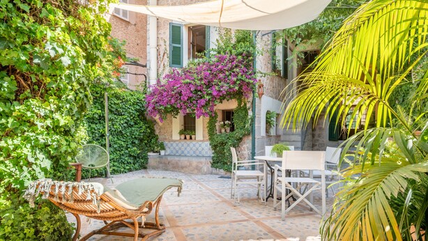 A patio with wicker furniture, a table, chairs, and a hanging planter with flowers. - Spacious townhouse in the heart of Sóller. (Soller)