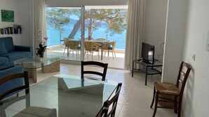 Een woonkamer met een glazen tafel, een blauwe bank en een tv op een dressoir.