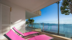 Un balcón con dos sillones reclinables rosa, barandilla de vidrio y vista al mar.