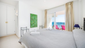 Habitación de hotel con cama, una silla, una mesa, un cuadro y un balcón con vistas.