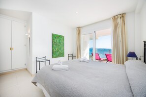 A hotel room with a bed, a chair, a table, a painting, and a balcony with a view. - Apartment Catalina 2B tres dormitorios by the Beach with Terrace & Wi-Fi (Puerto Pollensa)