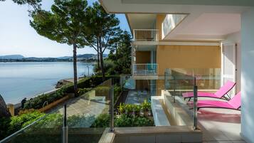 Un apartamento moderno con balcón de vidrio con vistas al agua, un balcón en el segundo piso y una terraza con plantas en macetas.