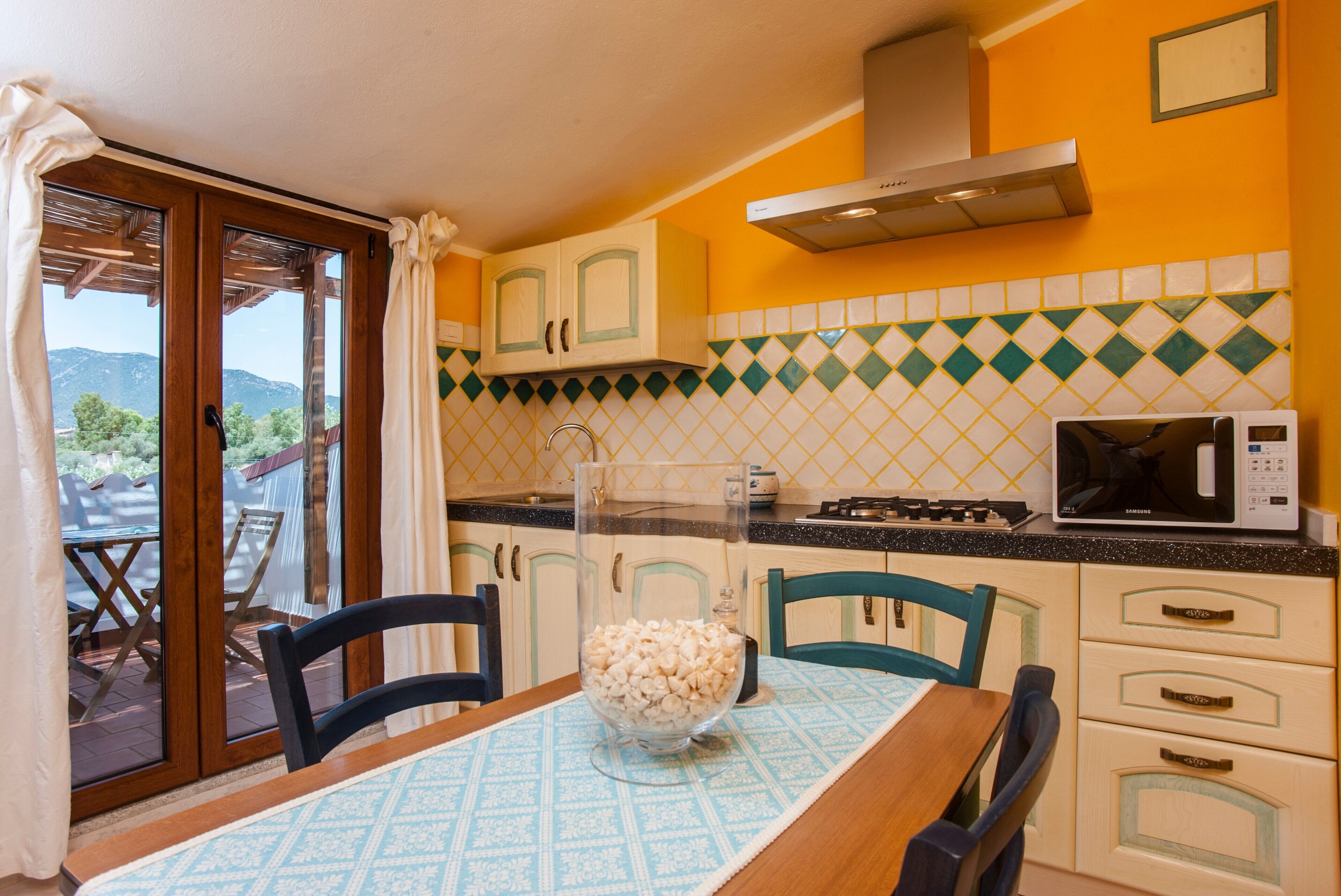 Una cocina con mesa, sillas, microondas y vistas a través del ventanal.
