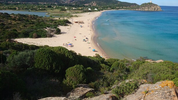 Una playa costera con aguas cristalinas, una orilla arenosa y montañas al fondo.