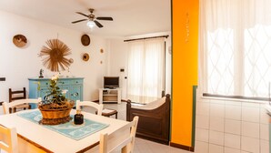 Un comedor con una mesa, sillas, un ventilador de techo, un televisor y una ventana con cortinas.