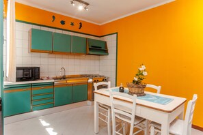 Cozinha com armários verde-água, bancada branca e mesa de jantar com cadeiras.