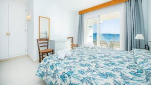 Une chambre à coucher avec un lit, un bureau, une chaise, un miroir et une vue sur la mer.