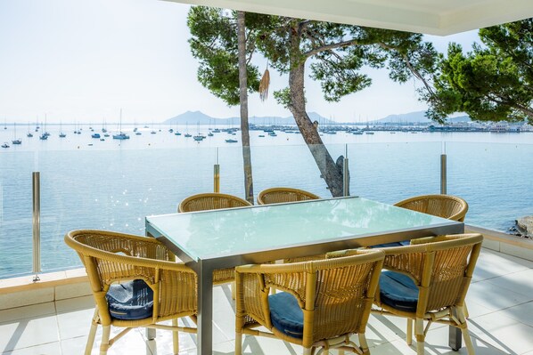 Une table et des chaises placées au bord de l’eau, avec vue sur les bateaux et les montagnes.