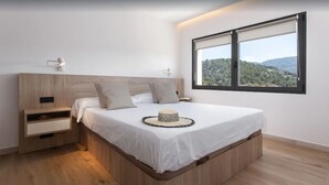 Une chambre à coucher moderne avec une tête de lit en bois, un grand lit, une table de chevet, une lampe de chevet et une fenêtre donnant sur un paysage vallonné.