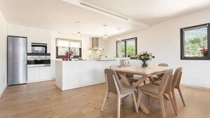 Une cuisine moderne avec des meubles blancs, un îlot central et un coin repas doté de chaises en bois.