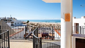 En balkon med udsigt over stranden, en hvid bygning og et gelænder af metal.