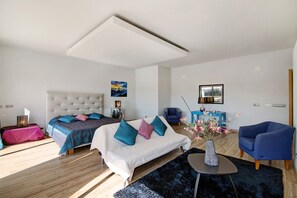 A modern bedroom with a large bed, a desk, a chair, and a vase with flowers.