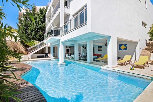 A modern building with a swimming pool, outdoor seating, and a staircase leading to an upper level.