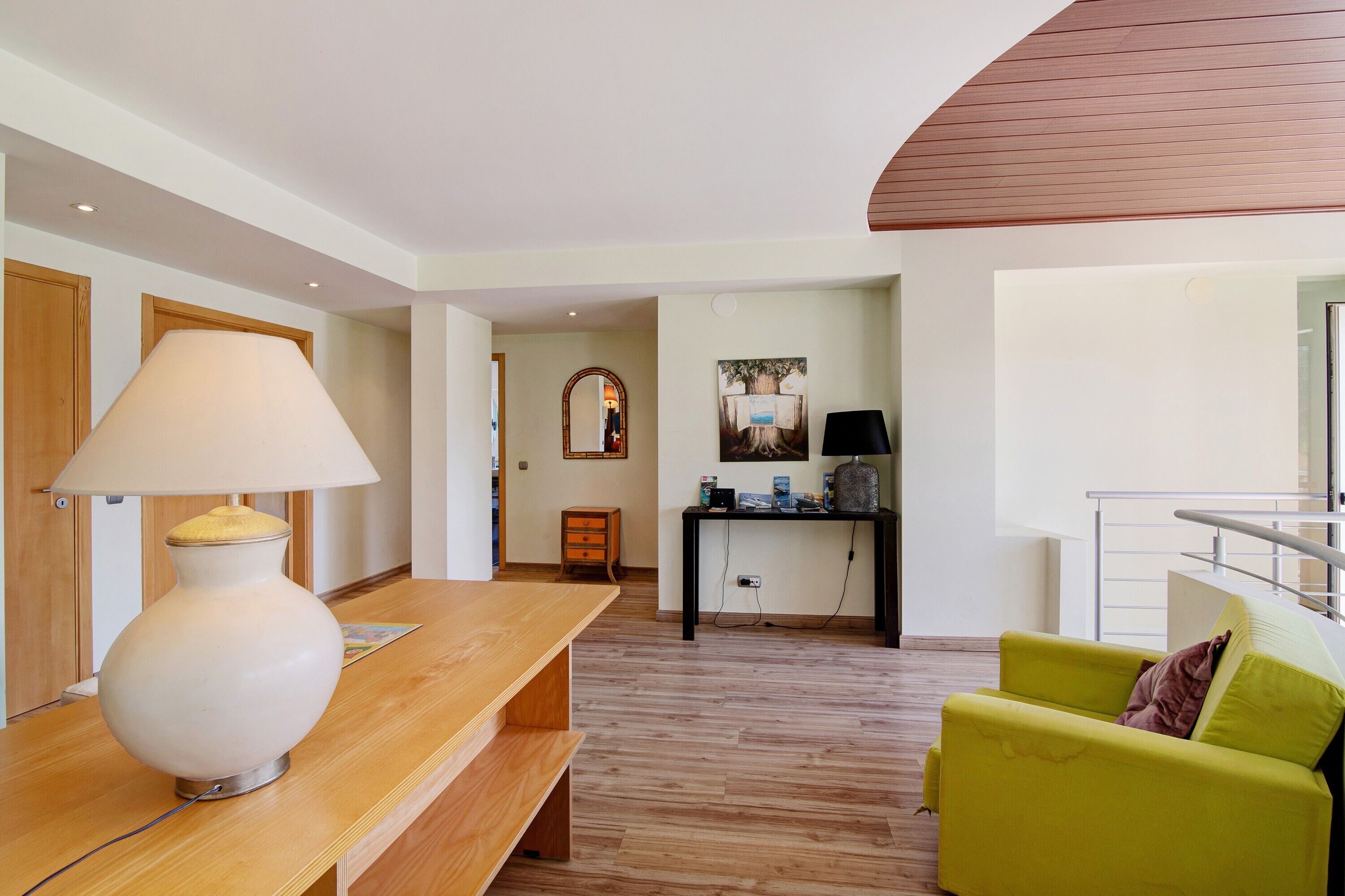 A modern living room with a wooden bench, a green sofa, a lamp, a small table, and a mirror.