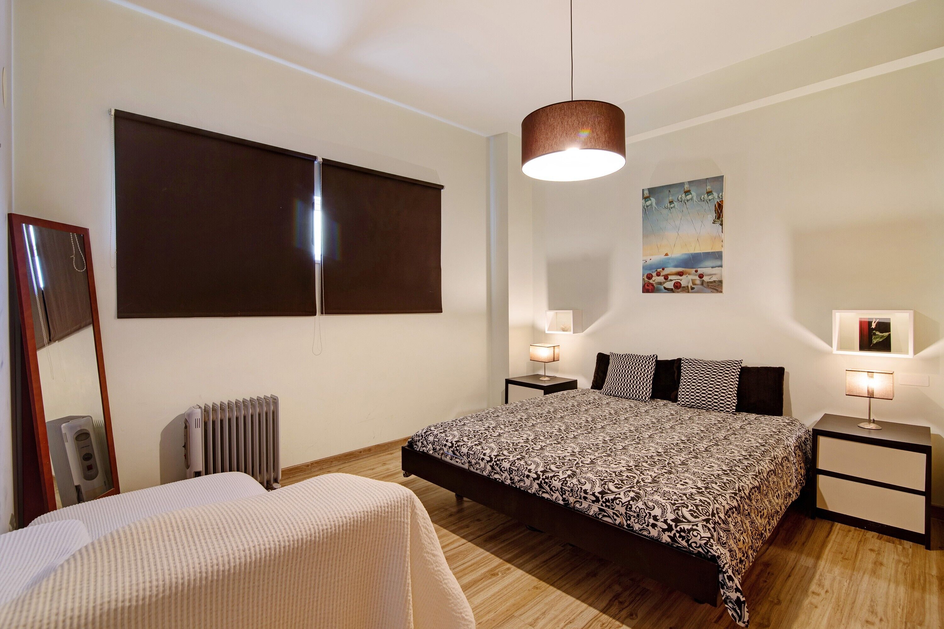 Ein Schlafzimmer mit Bett, Nachttischen, Heizkörper, Pendelleuchte und einem Bild an der Wand.