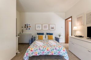 Een slaapkamer met een bed, nachtkastjes, een radiator, een televisie en ingelijste foto’s aan de muur.