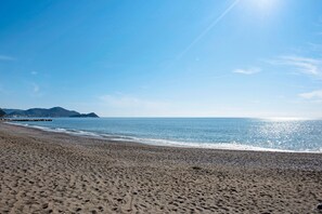 A beach with a clear sky, calm sea, and distant mountains.