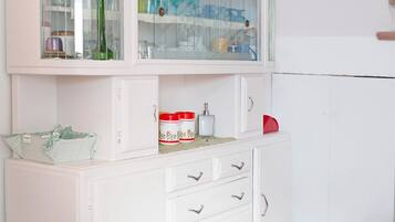 Une cuisine avec des meubles blancs, une étagère supérieure à façade en verre où sont rangés de la vaisselle, et un objet rouge sur l’étagère inférieure.