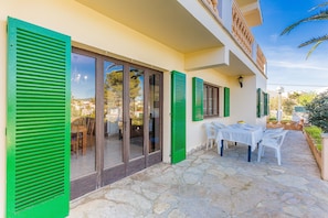 Un edificio con patio de piedra, contraventanas verdes y una mesa lista para comer.
