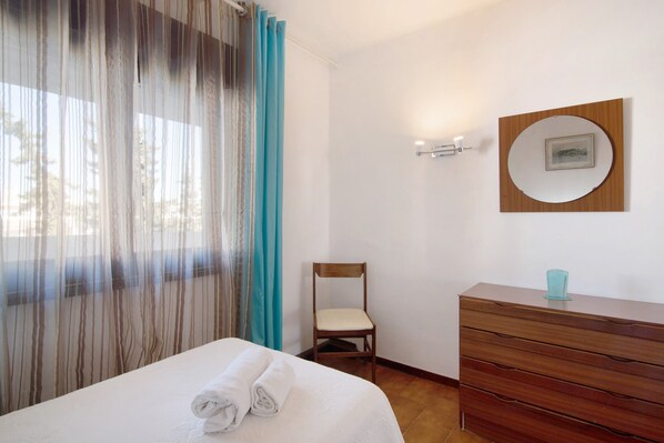 Une chambre d’hôtel comprenant un lit, une commode en bois, une chaise, une fenêtre avec des rideaux et un miroir fixé au mur.