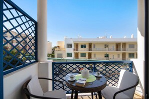Un balcon avec une table préparée pour le thé, une chaise et une vue sur un immeuble doté de nombreux balcons.