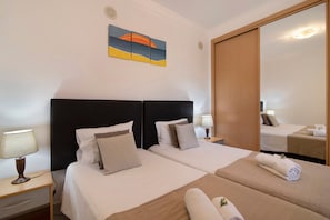 Une chambre d’hôtel avec deux lits, une table de chevet avec une lampe, un tableau au mur et un miroir qui reflète la pièce.
