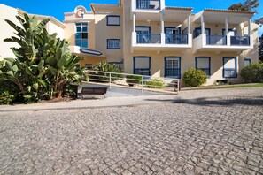Un immeuble à plusieurs étages doté de balcons, une rue pavée et des plantes tropicales.