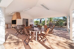 Une terrasse extérieure avec une table ronde et des chaises, un four en briques et une vue sur les arbres.