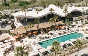 Un hôtel moderne doté d’une piscine, d’espaces de détente et de palmiers.