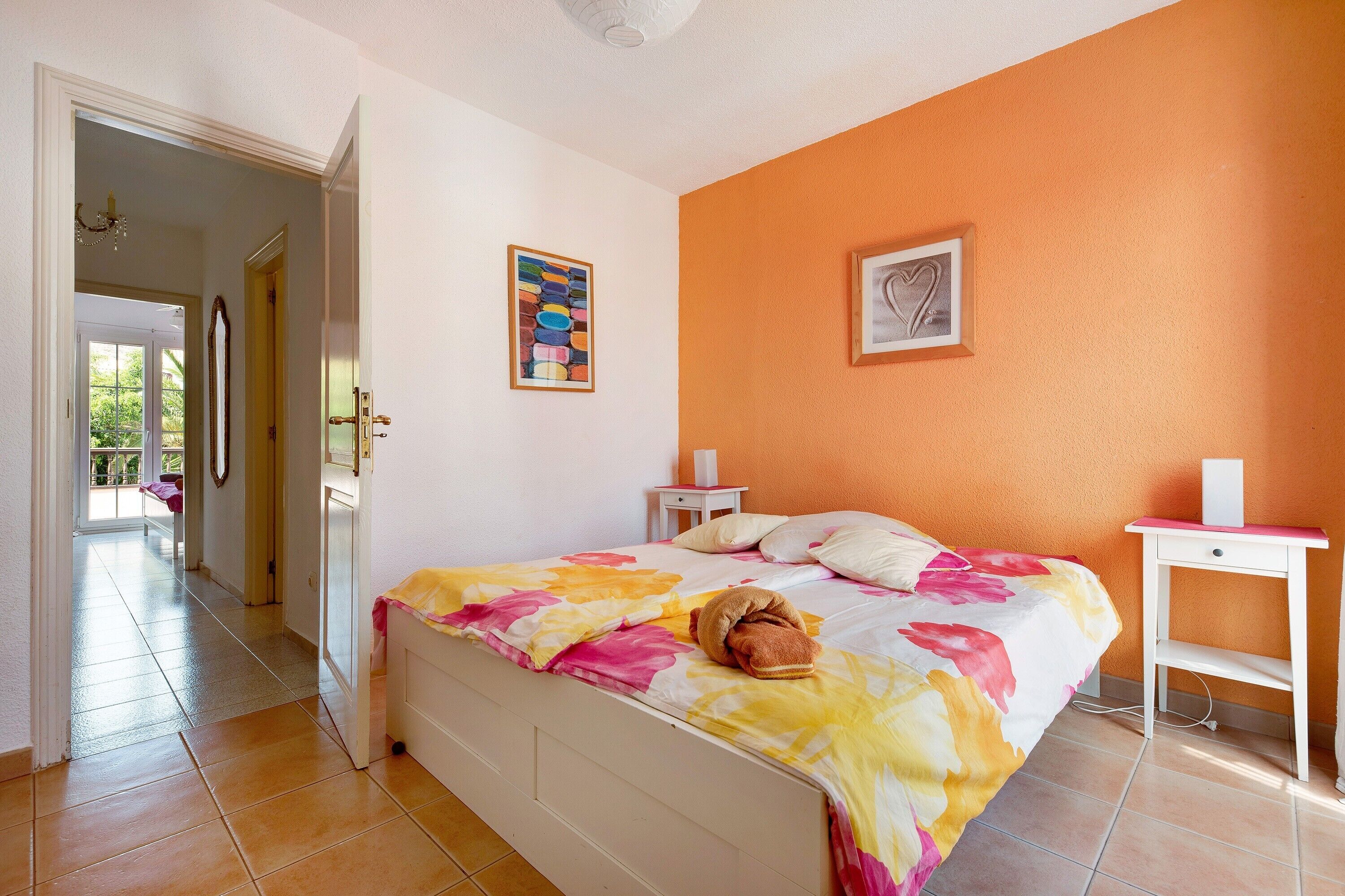 A bedroom with a bed, a nightstand, a bedside table, and a door leading to another room.