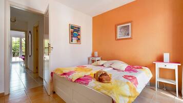 A bedroom with a bed, a nightstand, a bedside table, and a door leading to another room.