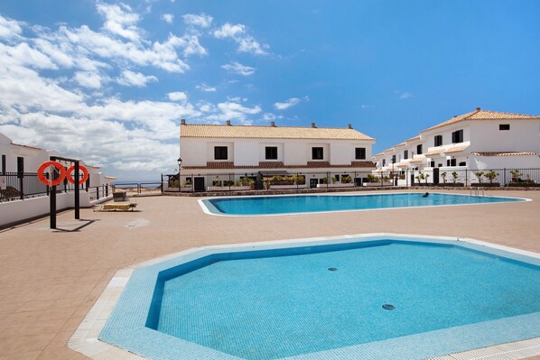 A swimming pool area with two pools, white buildings, and a clear sky. - Casa Dos Ángeles with Mountain Views, Pool, Air Conditioning, Wi-Fi, Garden & Terrace (Arona)