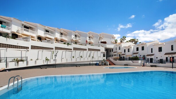 A swimming pool with a clear blue water surface, surrounded by white buildings with balconies and a clear sky. - Casa Dos Ángeles with Mountain Views, Pool, Air Conditioning, Wi-Fi, Garden & Terrace (Arona)