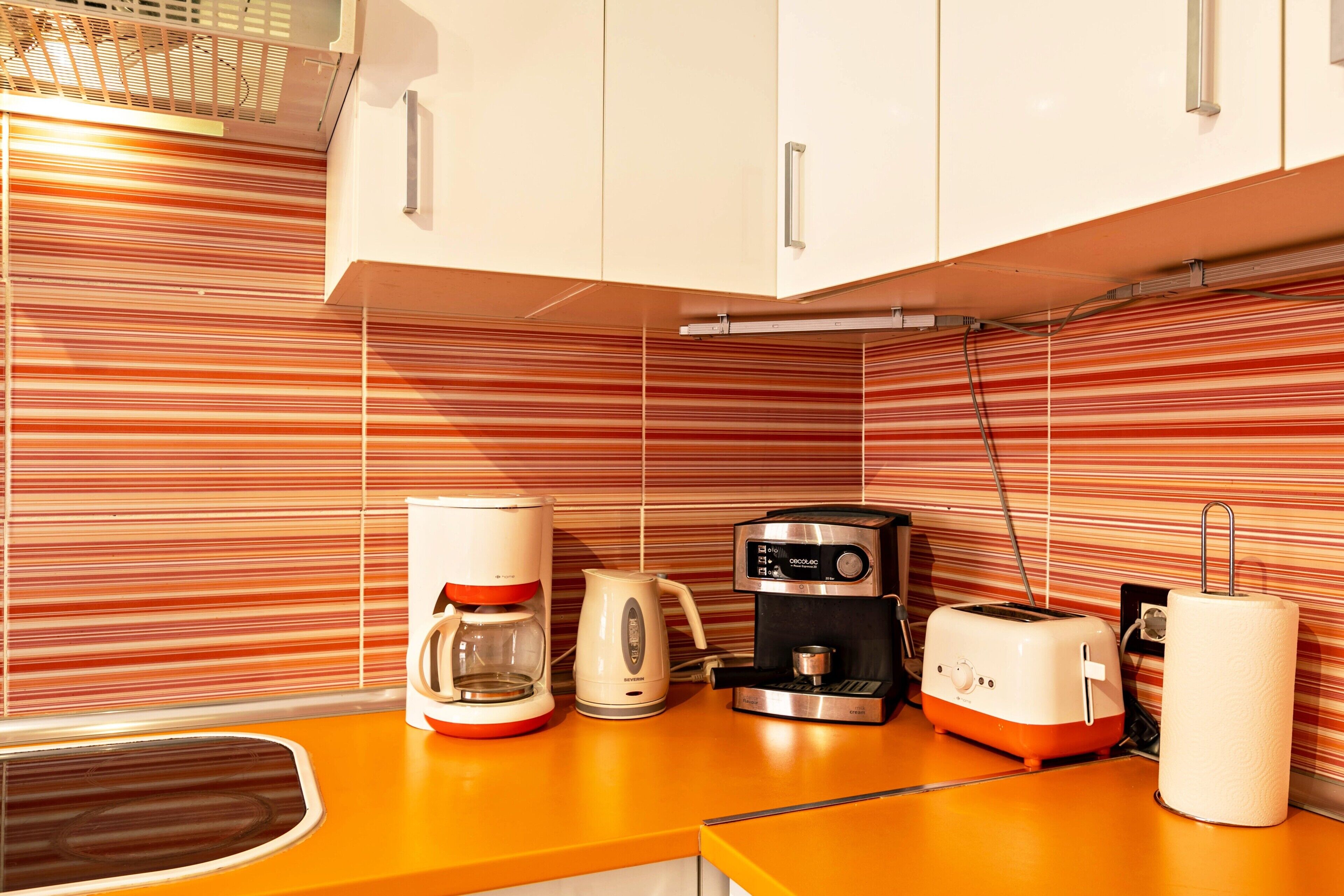 A kitchen with striped backsplash, a coffee maker, a toaster, and a kettle.