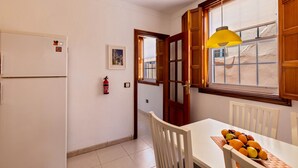 Une cuisine avec un réfrigérateur blanc, une porte en bois, une fenêtre donnant sur un beau paysage et une table avec des fruits.