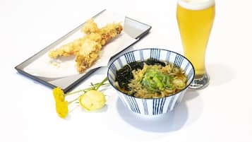 Un bol de ramen garni d’algues et d’oignons verts, un verre de bière et une portion de friture sur une table blanche.