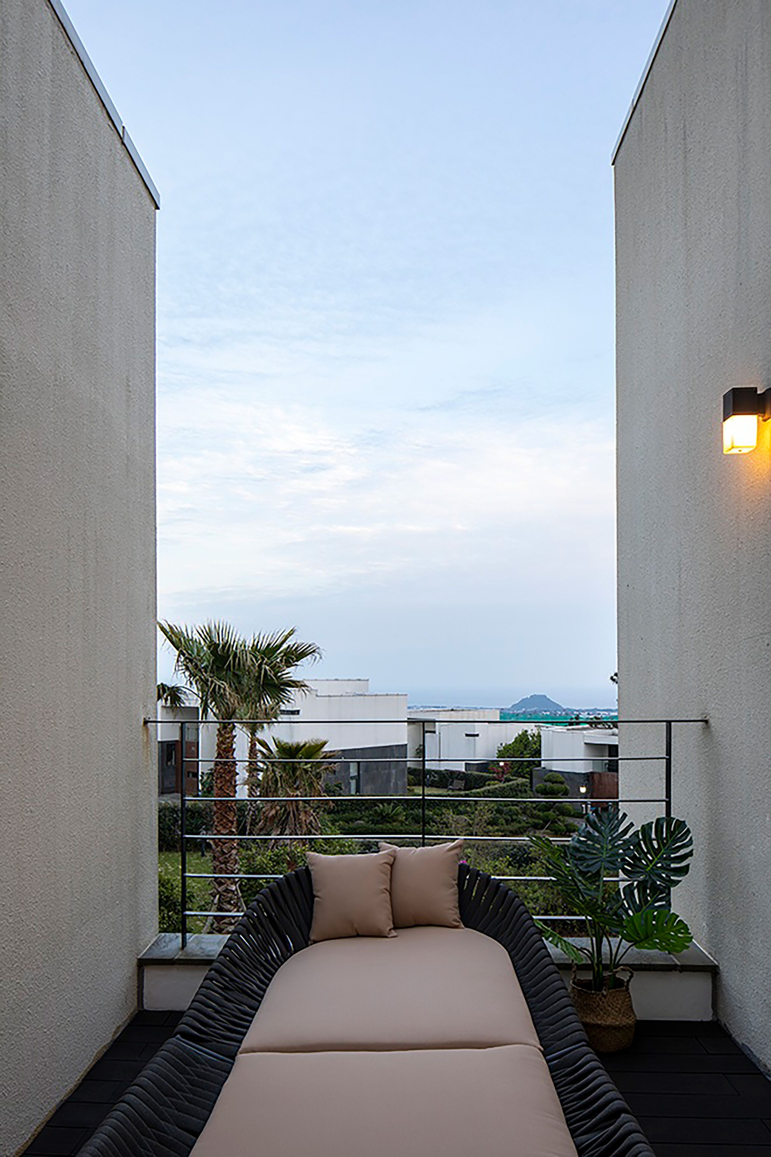 A balcony with a bed, a potted plant, and a view of the cityscape.