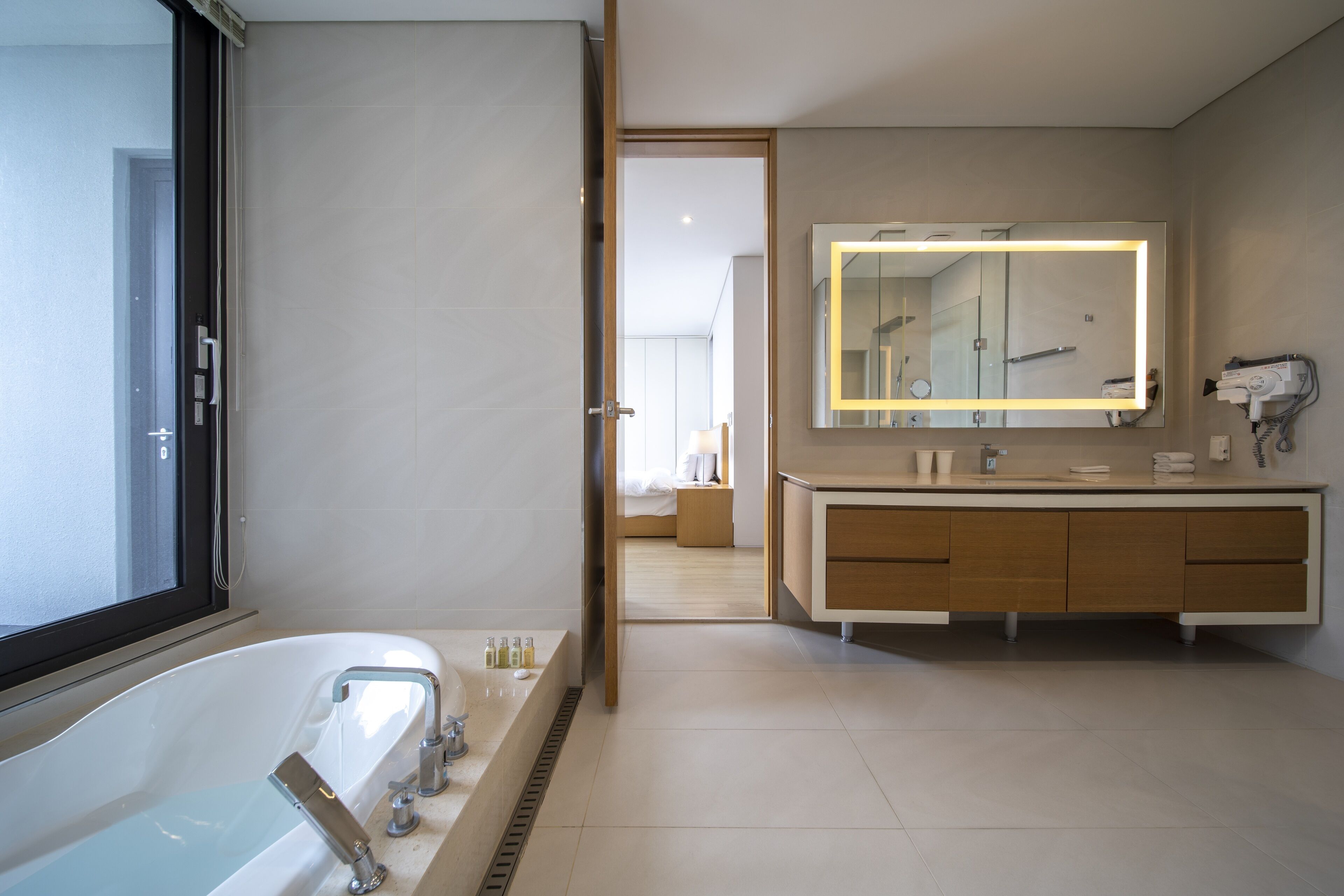 A modern bathroom with a large bathtub, a vanity with a mirror, and a hairdryer on the wall.