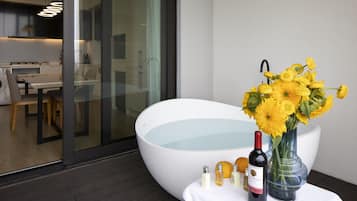 Une salle de bain moderne avec une grande baignoire, une douche en verre et une table sur laquelle sont disposés des articles de toilette et un vase de fleurs.