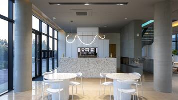 En moderne reception med en central ø, to runde borde med stole, store vinduer og en unik loftslampe.