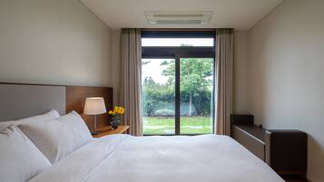 A hotel room with a large bed, a nightstand with a lamp and flowers, a TV, and a sliding glass door to the outside.