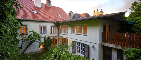 A two-story house with a red-tiled roof, a balcony, and a garden area.
